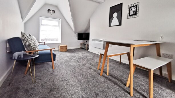 Une pièce moderne et bien éclairée, avec un plafond en pente, un bureau, une chaise, un téléviseur et un radiateur.
