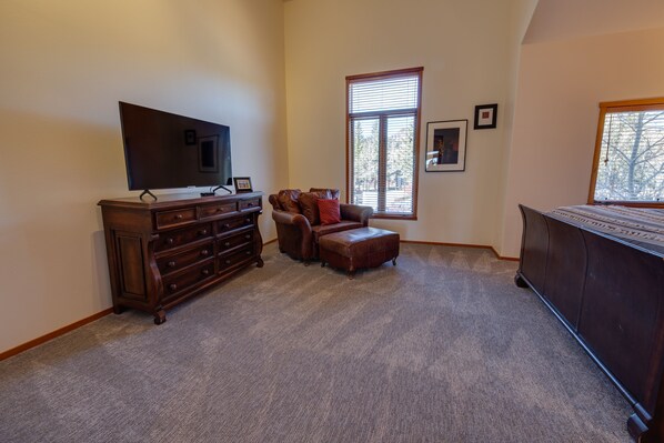Un salón amplio con una gran televisión de pantalla plana, un sofá de cuero marrón, un mueble de madera y un amplio ventanal que proporciona luz natural.
