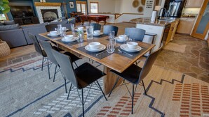 Un comedor con una mesa de madera dispuesta para seis personas, rodeada de sillas grises. Se ve una mesa de billar al fondo.