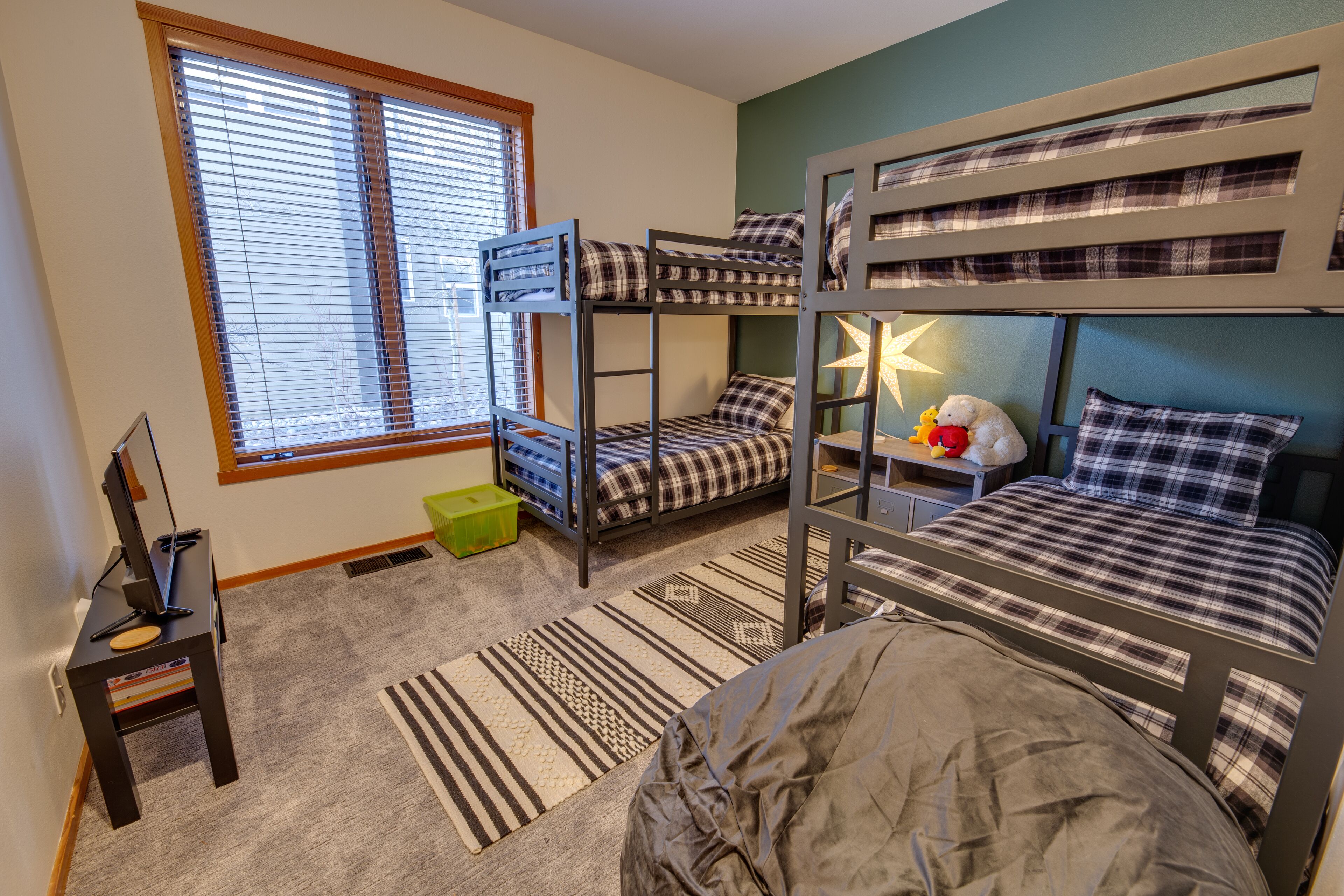 A bunk bed room with a desk, a lamp, and a window with blinds.