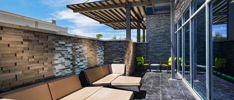 An outdoor seating area with a modern design, featuring a mix of seating arrangements and a glass wall providing a view of the sky.