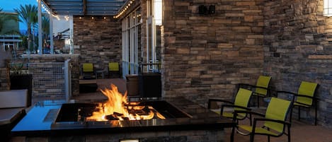 An outdoor seating area with a stone wall, a fire feature, and chairs.