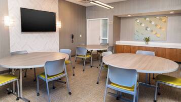 A conference room with round tables and chairs, a flat-screen TV, and a decorative wall piece.