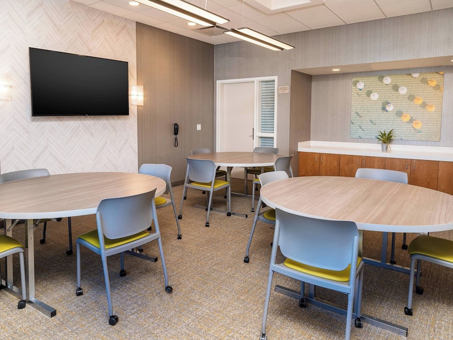 A conference room with round tables and chairs, a flat-screen TV, and a decorative wall piece.