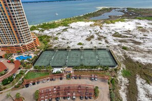 A multi-story hotel with a tennis court complex, a swimming pool, and a parking area.