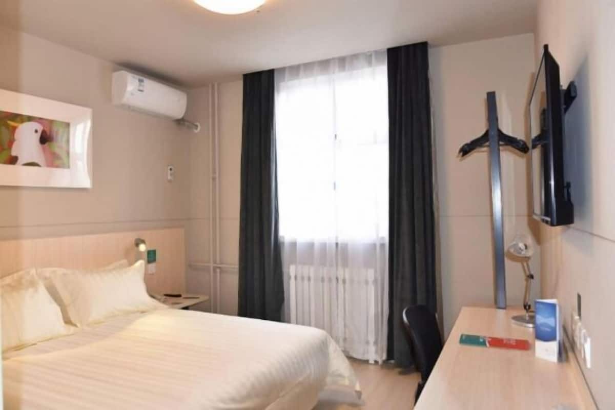A hotel room with a bed, a desk, a chair, a TV, and a window with curtains.
