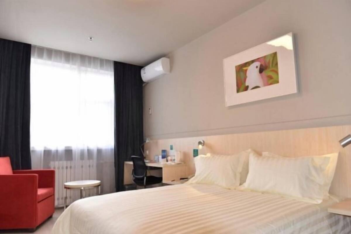 A hotel room with a bed, a desk, a chair, and a window with curtains.