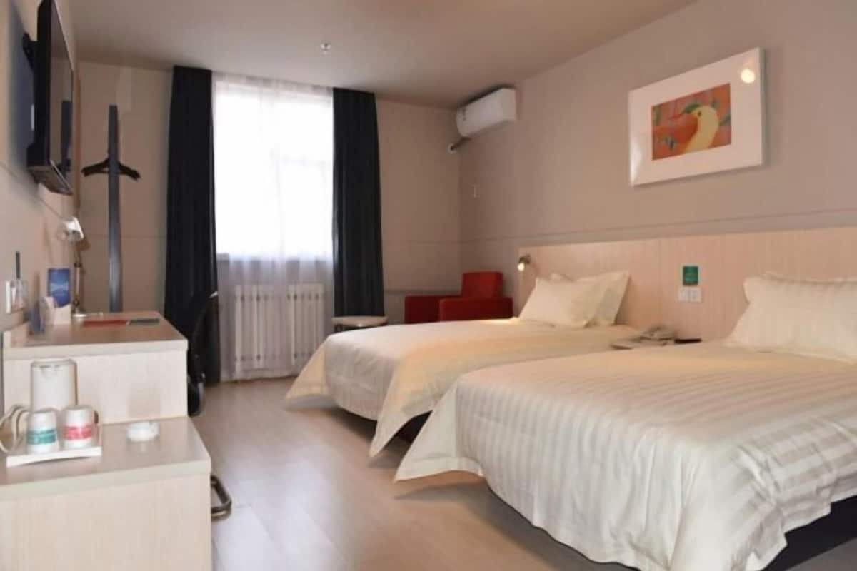 A hotel room with two beds, a desk with a chair, a TV, and a window with curtains.