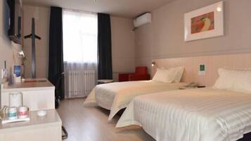 A hotel room with two beds, a desk with a chair, a TV, and a window with curtains.