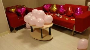 Una habitación con un sofá rojo decorado con globos con forma de corazón y una mesita con globos rosas.