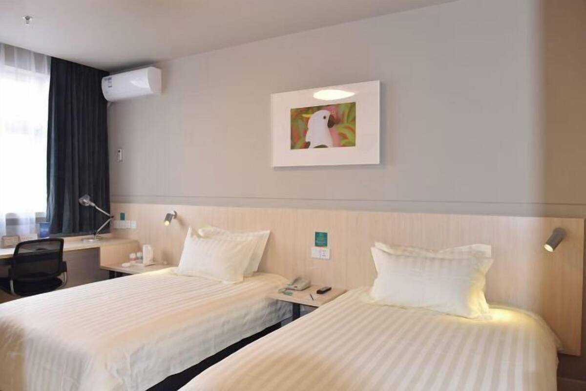 A hotel room with two beds, a desk, a chair, an air conditioning unit, and a framed picture on the wall.