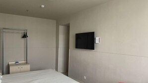 Habitación de hotel con cama, mesita de noche, espejo, televisor montado en la pared y una silla roja.