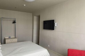 Ein Hotelzimmer mit einem Bett, einem kleinen Nachttisch, einem Spiegel, einem an der Wand befestigten Fernseher und einem roten Sessel.