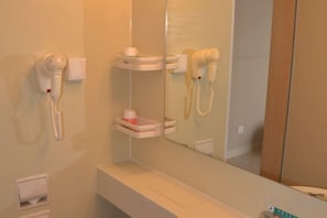 Un baño con secador de pelo montado en la pared, un espejo y un estante con artículos de aseo.