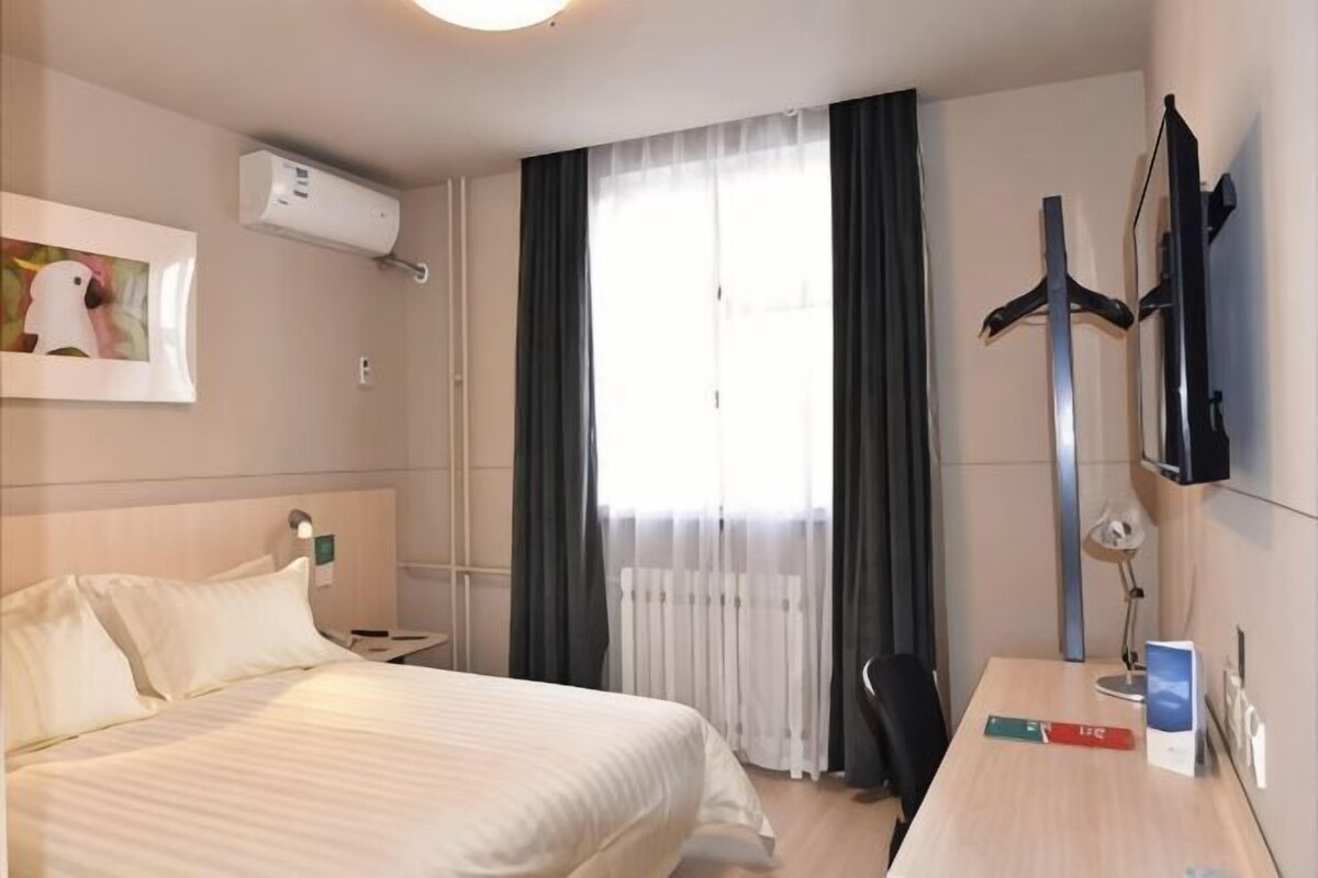 Una habitación de hotel con cama, escritorio, silla, televisor y ventana con cortinas.