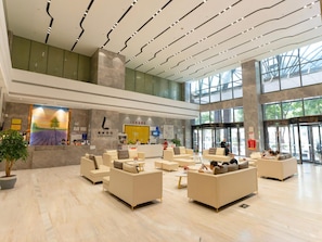 A spacious lobby with multiple seating areas, a reception desk, and a large window providing natural light.