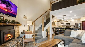 Un vaste espace de vie doté d’une cheminée, d’un escalier menant à l’étage supérieur, d’un coin repas et d’une cuisine.