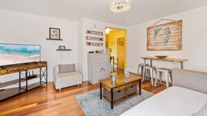 A modern living room with a wooden coffee table, a sofa, a TV, and a dining area with stools.