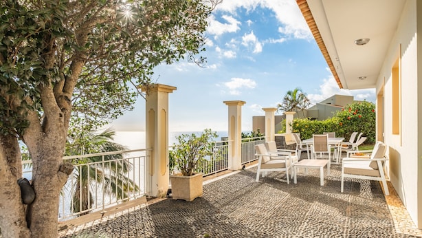 An outdoor patio with a stone floor, white furniture, and a view of the sea.