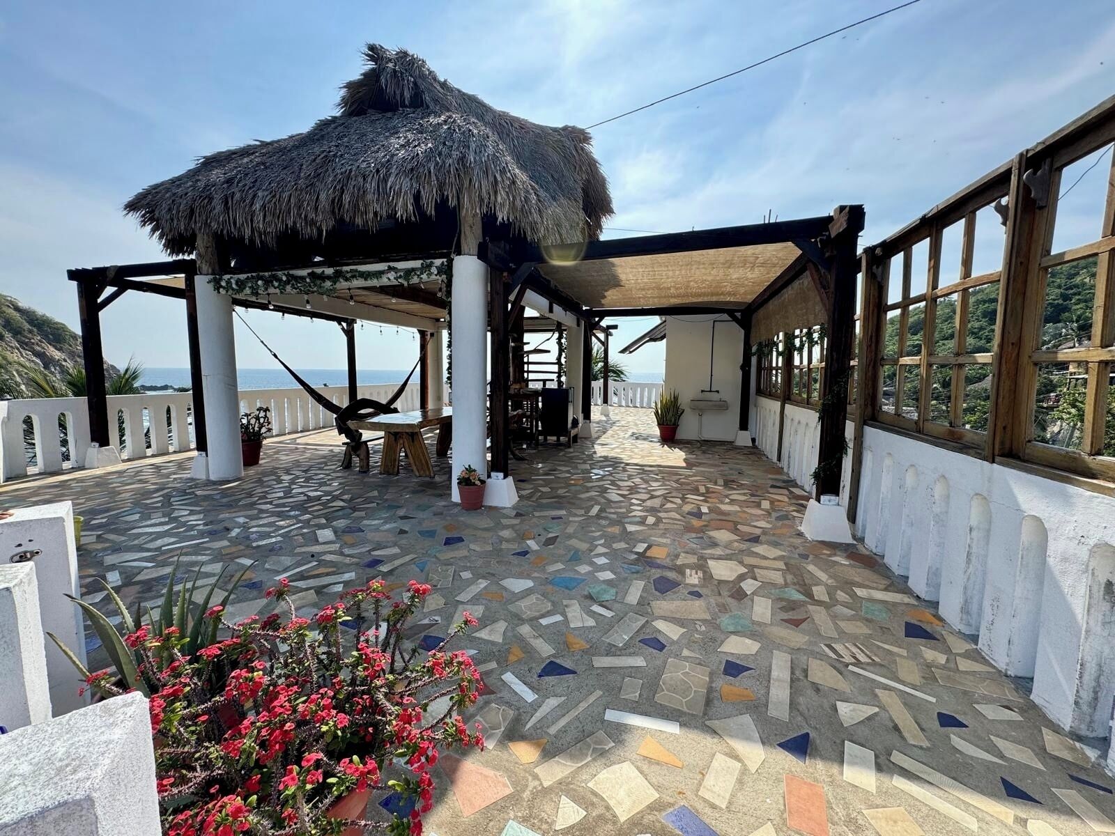 Un espace extérieur abrité, doté d’un toit de chaume, d’un sol recouvert de mosaïques et offrant une vue sur la mer.