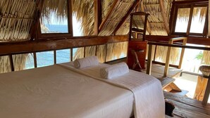 A bed with white linens, a wooden headboard, and a view of the ocean through a thatched roof structure. - Casa El Delfin, 3rd Floor Bungalow - Estacahuite (Estacahuite)
