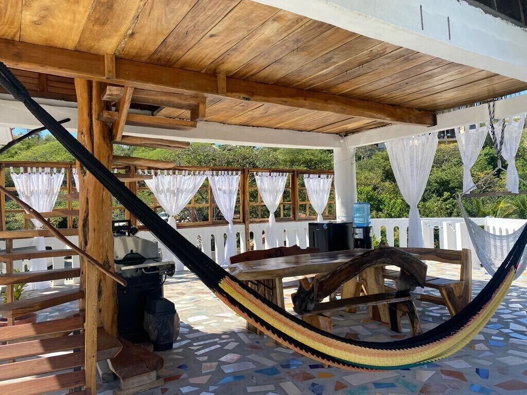 A covered outdoor area with a wooden table and chairs, a hammock, and a white fence.