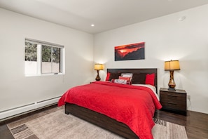 A bedroom with a large bed, two bedside tables with lamps, a window, and a painting on the wall.