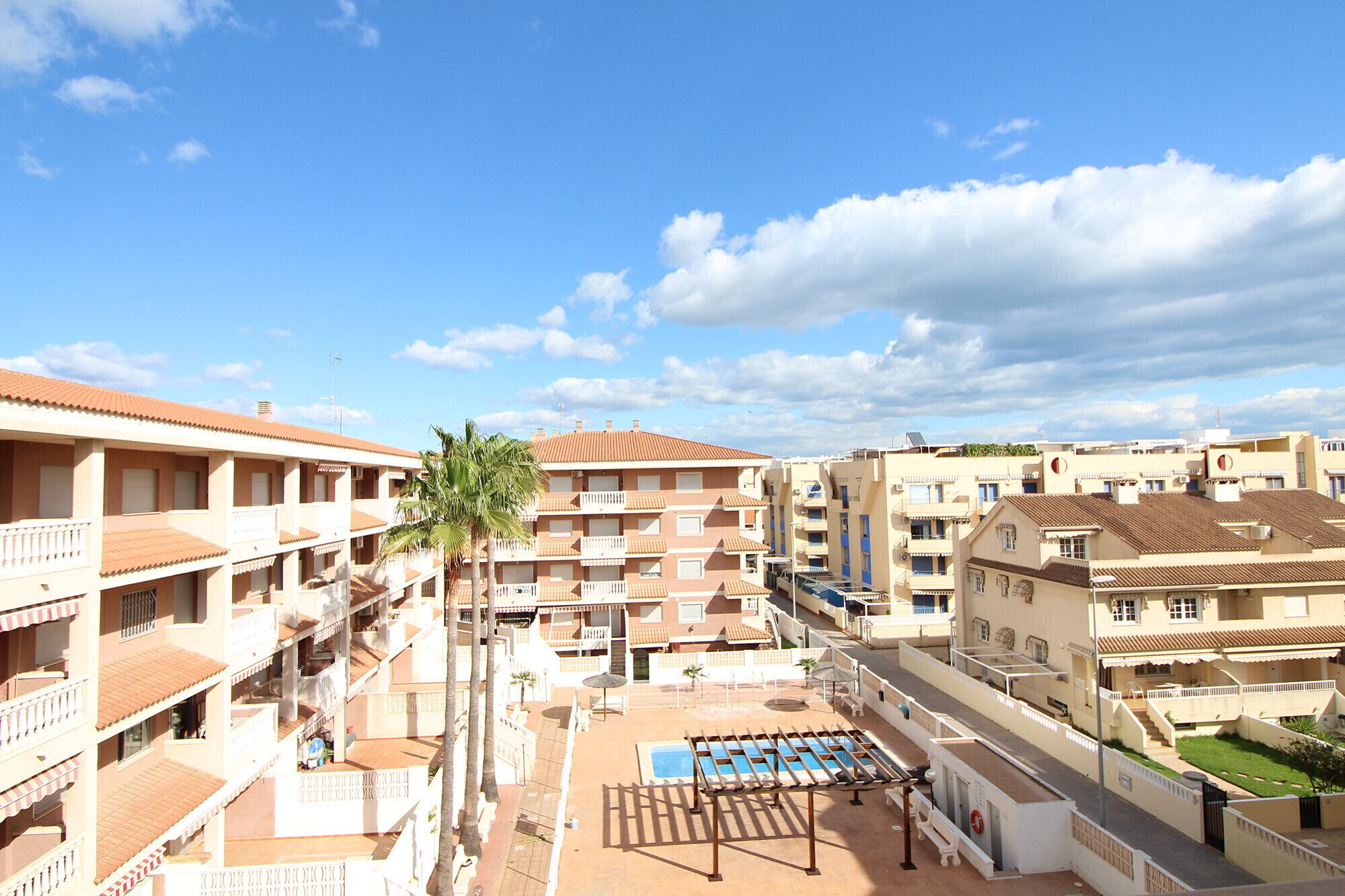 A multi-story hotel with balconies, a swimming pool, and a clear sky.