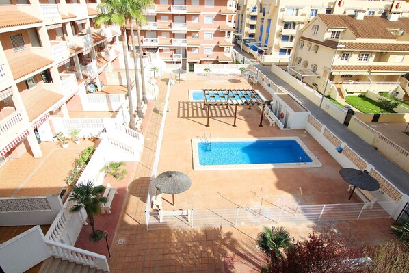A rooftop pool area with a rectangular pool, sun loungers, and a pergola.