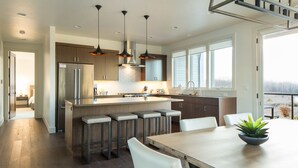 Una cocina moderna con una isla central, taburetes de bar, iluminación colgante y vistas a un paisaje nevado a través de amplios ventanales.