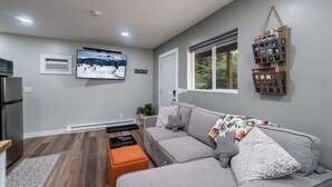 Een moderne woonkamer met een grijze bank, een flatscreen televisie, een houten salontafel en een wandplank met boeken.