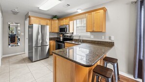 A modern kitchen with granite countertops, stainless steel appliances, wooden cabinets, and a central island with bar stools. - Less than 5 Mins to the Gulf, Pool, Beach Service Included! - Pineapple Paradise at St. Martin (Destin)