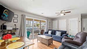 A spacious living room with a wooden dining table, blue and grey sofas, and a ceiling fan. - Less than 5 Mins to the Gulf, Pool, Beach Service Included! - Pineapple Paradise at St. Martin (Destin)