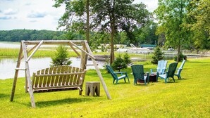A wooden swing set, green chairs, and a small table on a grassy area near a body of water. - Comfortable & clean cabin on beautiful 3rd Crow Wing Lake in Hubbard County MN. (Nevis)