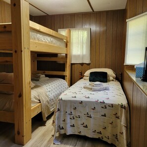 A bunk bed room with a wooden floor, a single bed with a patterned duvet, and a window with blinds. - Comfortable & clean cabin on beautiful 3rd Crow Wing Lake in Hubbard County MN. (Nevis)