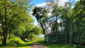 A dirt path leading to a small, single-story cabin surrounded by lush greenery and trees. - Comfortable & clean cabin on beautiful 3rd Crow Wing Lake in Hubbard County MN. (Nevis)