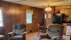A cozy living room with wooden walls, a dining table with chairs, and a kitchen area with a stove and refrigerator. - Comfortable & clean cabin on beautiful 3rd Crow Wing Lake in Hubbard County MN. (Nevis)