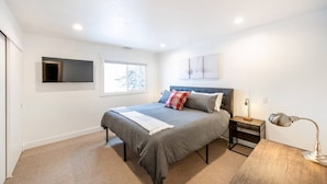 A bedroom with a bed, a bedside table, a lamp, a TV mounted on the wall, and a window. - Cozy Cottage in downtown PC. Steps to mountain! (Park City)