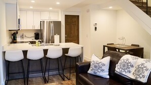 A modern kitchen with white cabinets, a stainless steel refrigerator, and a bar area with stools. - Cozy Cottage in downtown PC. Steps to mountain! (Park City)