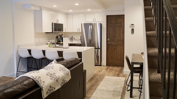 A modern kitchen with white cabinets, stainless steel appliances, and a central island with bar stools. - Cozy Cottage in downtown PC. Steps to mountain! (Park City)