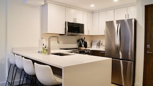 A modern kitchen with white cabinetry, a stainless steel refrigerator, a microwave, and a sink. - Cozy Cottage in downtown PC. Steps to mountain! (Park City)