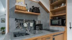 Cozinha compacta com pia embutida, cafeteira, micro-ondas e prateleiras de madeira acima do balcão.