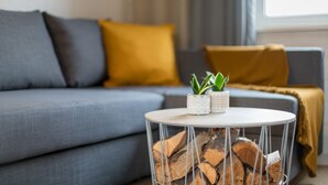 Uma sala de estar moderna com um sofá cinzento, um cobertor amarelo e uma pequena mesa redonda com uma planta e lenha.