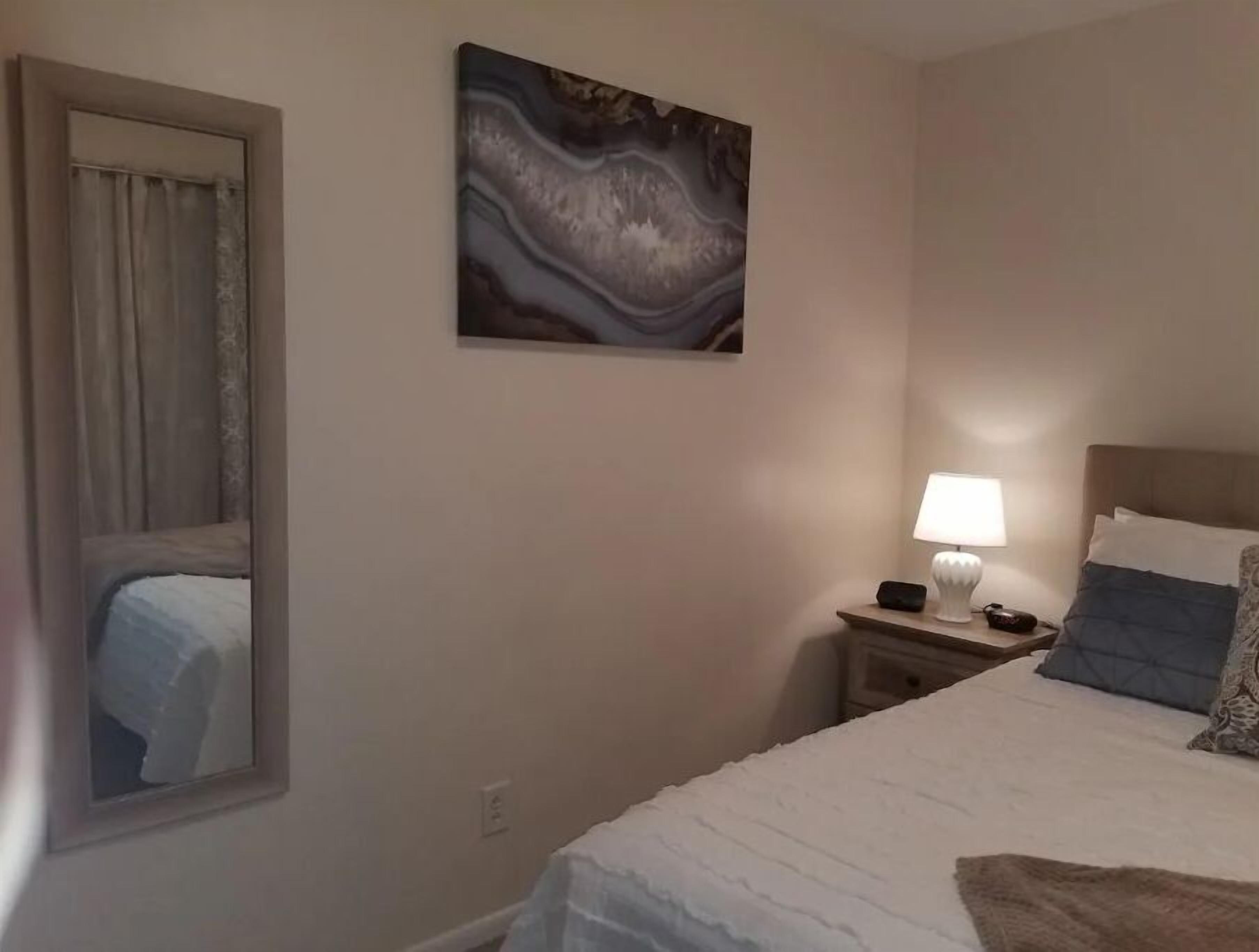 Habitación de hotel con cama, mesita de noche con lámpara, un cuadro en la pared y una ventana con cortinas.
