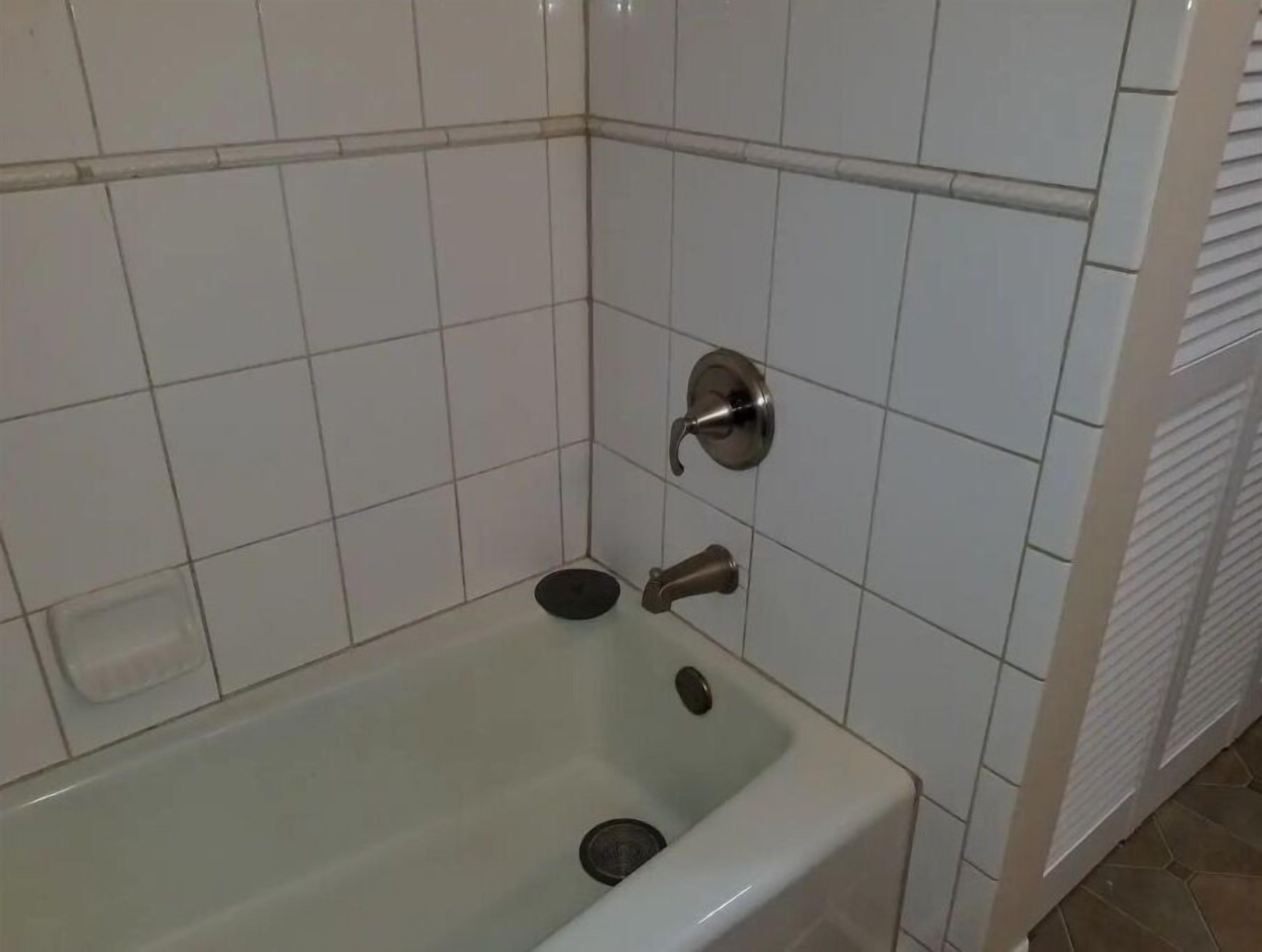 Ein Badezimmer mit weiß gefliestem Duschbereich, einer Badewanne und einem WC.