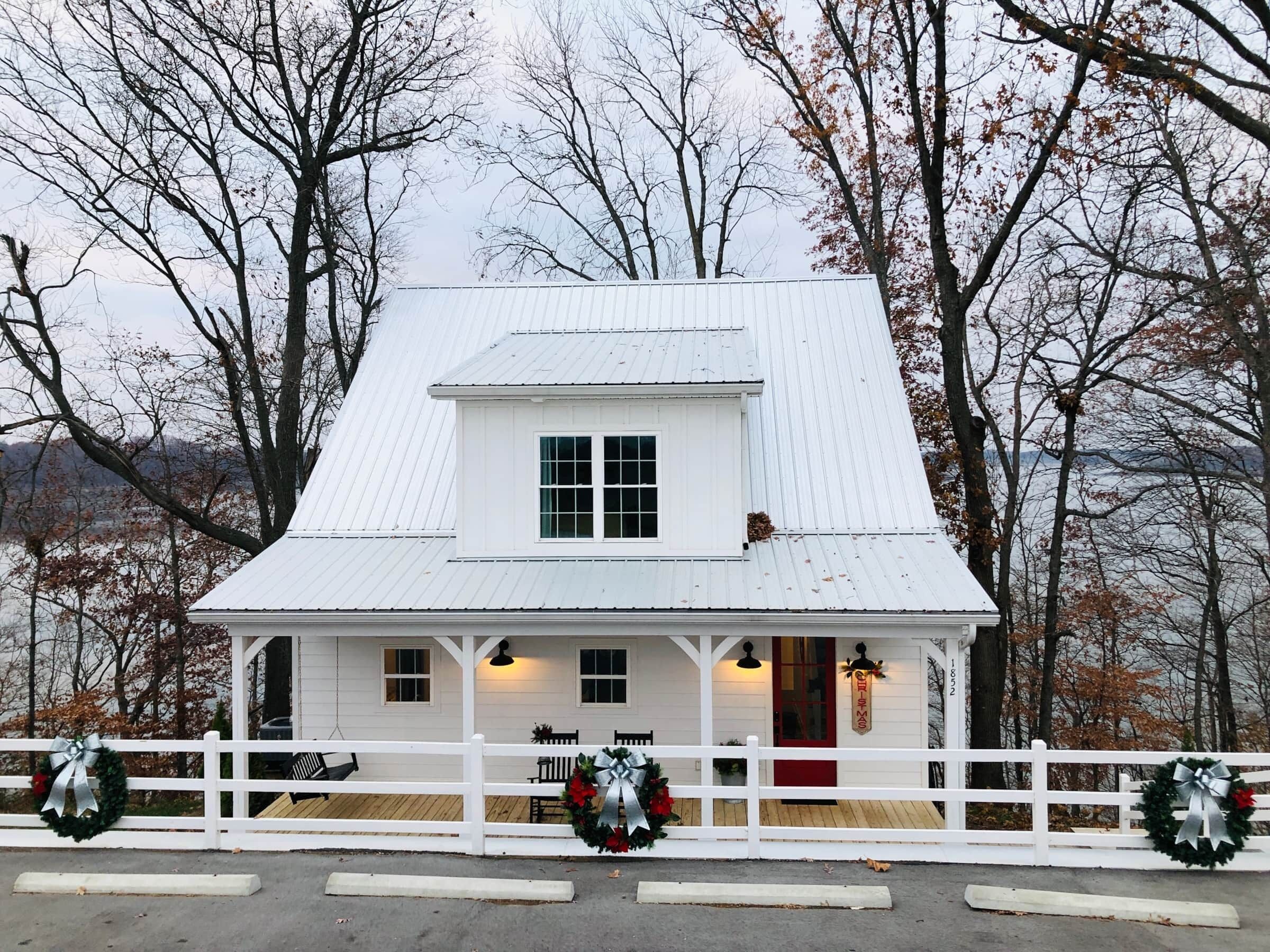 A white house with a gabled roof, a front porch, and a white picket fence.