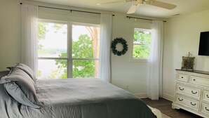 A bedroom with a bed, large windows, a ceiling fan, a dresser, and a wall-mounted TV. - the Red Door Lakeside (Allen County)