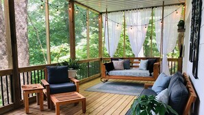 A wooden deck with a swing seat, a cushioned bench, and a small table with a plant.