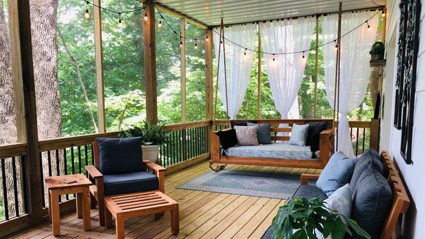 A wooden deck with a swing seat, a cushioned bench, and a small table with a plant. - the Red Door Lakeside (Allen County)