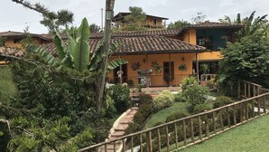 Una casa de dos pisos con techo de tejas, rodeada de exuberante vegetación y un césped cuidado.